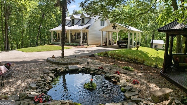 view of green lawn featuring a small pond and covered porch