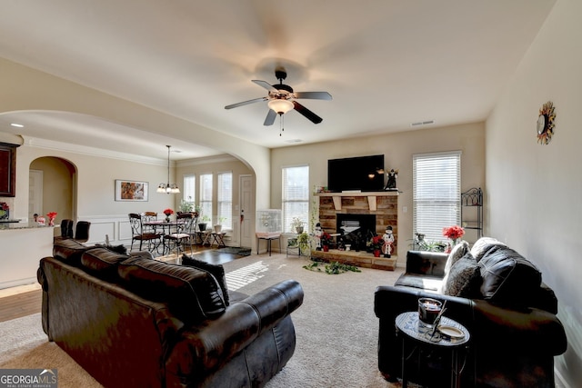 carpeted living room featuring ceiling fan with notable chandelier, ornamental molding, and a fireplace