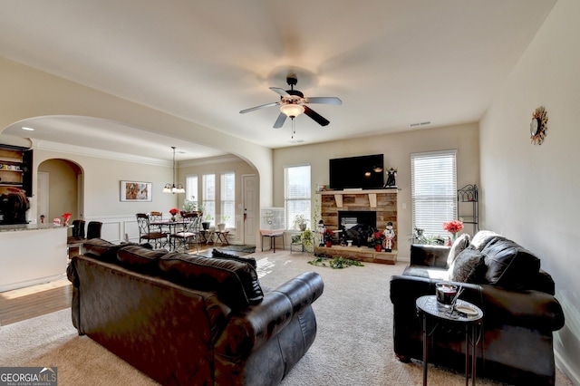 carpeted living room featuring ceiling fan with notable chandelier, a stone fireplace, and ornamental molding