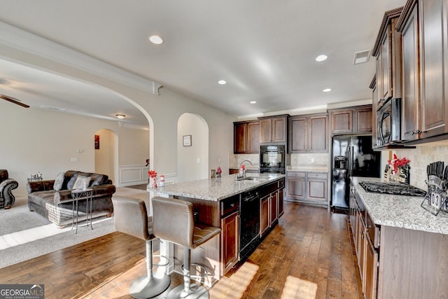 kitchen featuring light stone counters, black appliances, sink, a center island with sink, and dark hardwood / wood-style floors