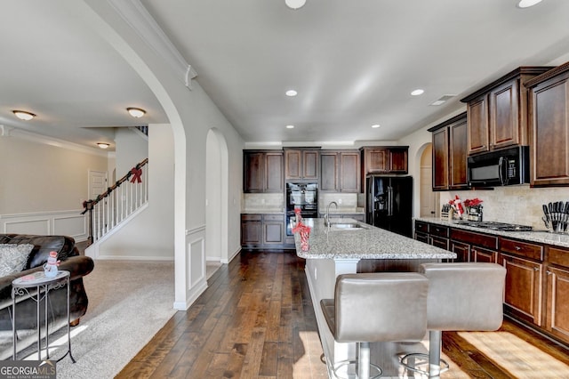 kitchen with backsplash, a kitchen island with sink, dark wood-type flooring, and black appliances