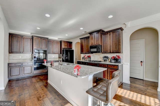 kitchen with black appliances, dark hardwood / wood-style floors, a kitchen island with sink, and tasteful backsplash