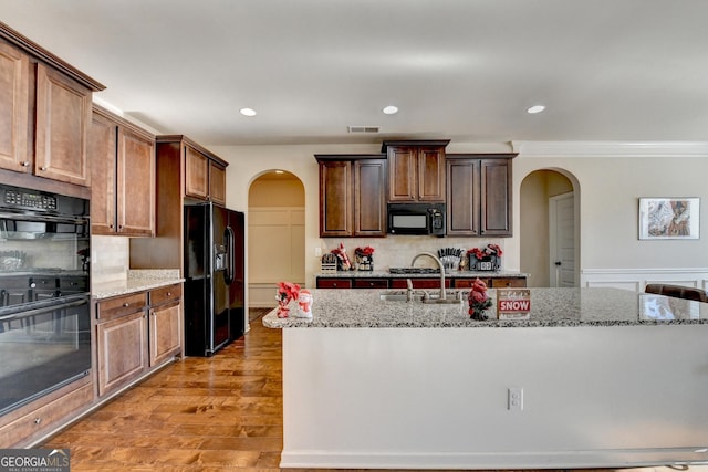 kitchen featuring light stone countertops, tasteful backsplash, light hardwood / wood-style flooring, a kitchen island with sink, and black appliances