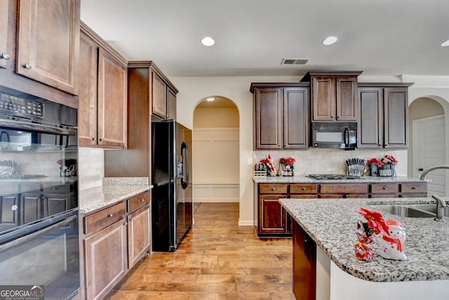 kitchen featuring light stone countertops, backsplash, sink, black appliances, and light hardwood / wood-style floors