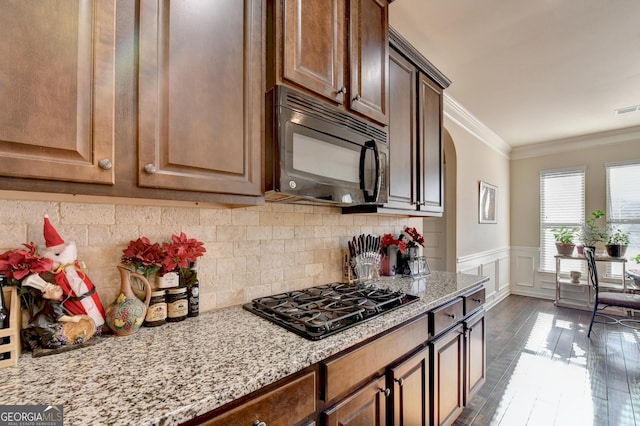 kitchen with dark wood-type flooring, black appliances, crown molding, decorative backsplash, and light stone countertops