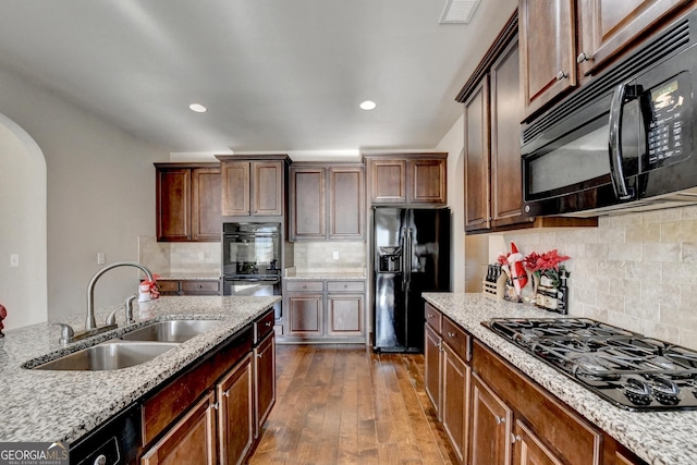 kitchen featuring sink, light stone counters, dark hardwood / wood-style flooring, decorative backsplash, and black appliances