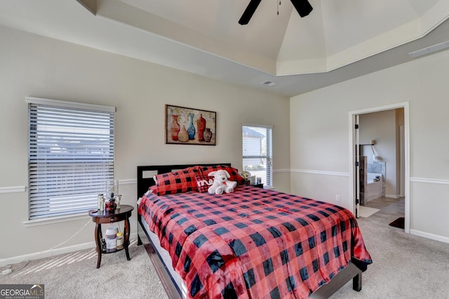 carpeted bedroom with a raised ceiling, connected bathroom, and ceiling fan