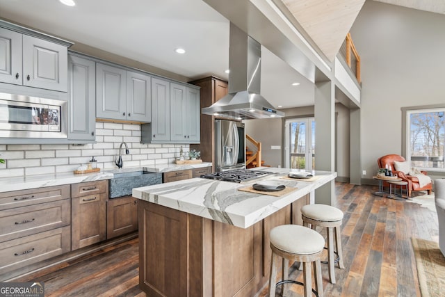 kitchen with appliances with stainless steel finishes, light stone countertops, island range hood, a kitchen island, and sink