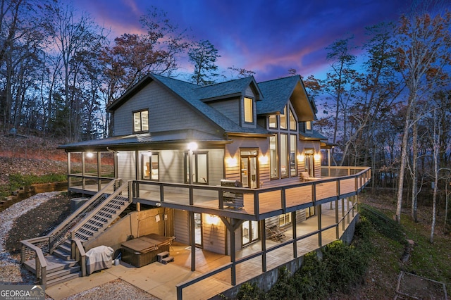 back house at dusk with a patio, a wooden deck, and a covered hot tub