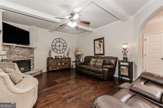 living room with ornamental molding, ceiling fan, beamed ceiling, dark hardwood / wood-style floors, and a stone fireplace