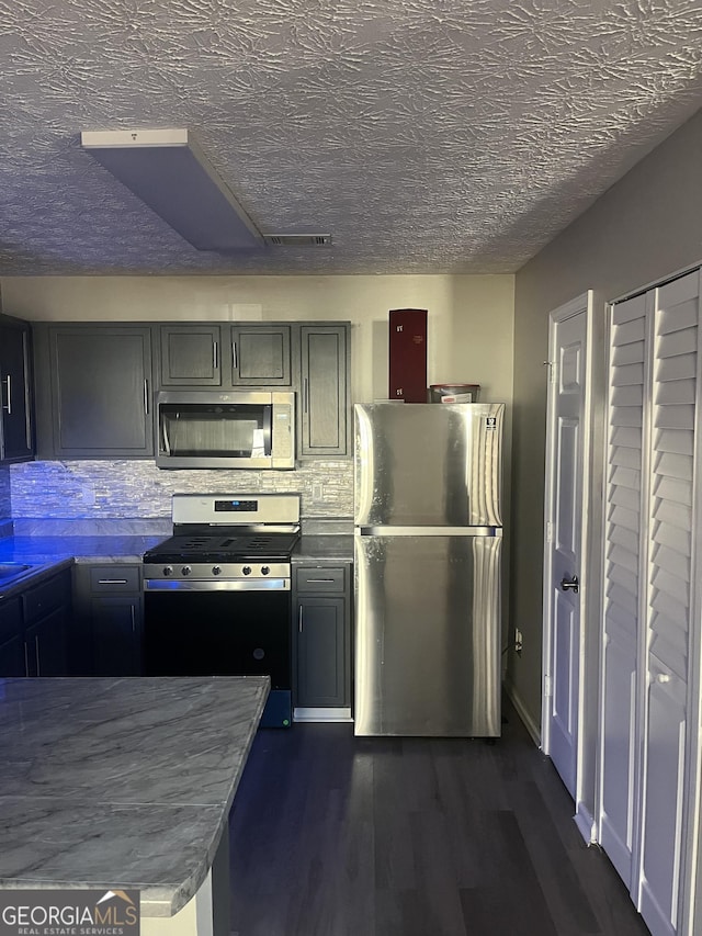 kitchen with dark wood-type flooring, gray cabinets, appliances with stainless steel finishes, a textured ceiling, and decorative backsplash