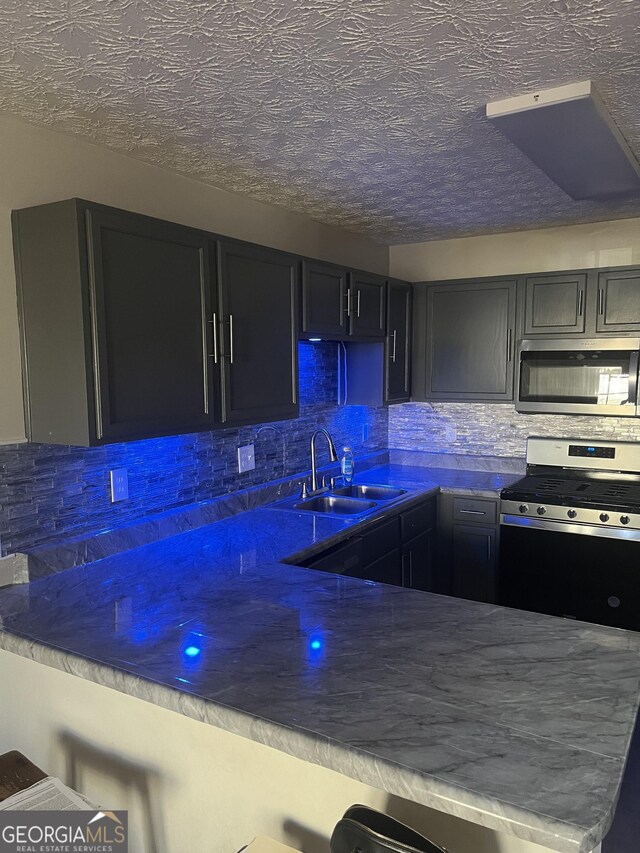 kitchen with a textured ceiling, backsplash, stainless steel appliances, and sink