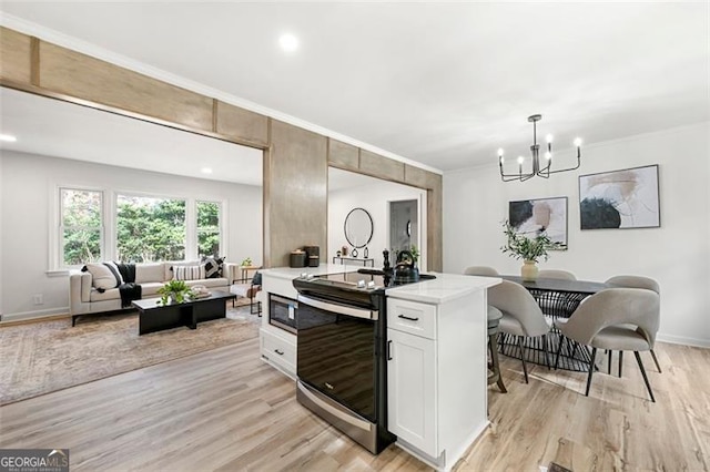 kitchen with light wood-type flooring, white cabinetry, hanging light fixtures, and appliances with stainless steel finishes