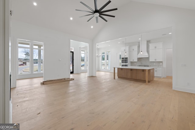 kitchen featuring open floor plan, high vaulted ceiling, premium range hood, and light wood-type flooring