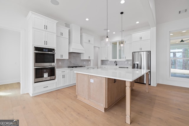 kitchen with stainless steel appliances, visible vents, white cabinetry, a kitchen island, and premium range hood