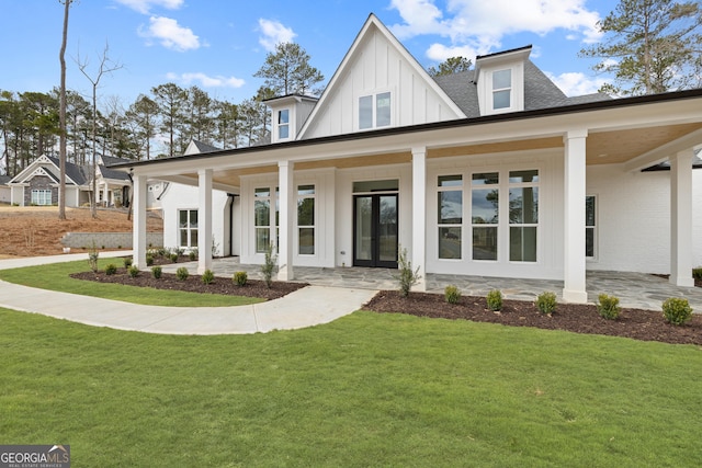 modern farmhouse style home featuring board and batten siding, a front yard, covered porch, and a shingled roof