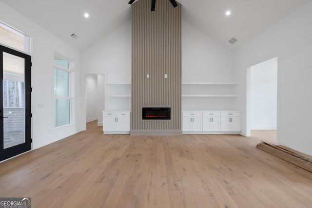 unfurnished living room with high vaulted ceiling, recessed lighting, visible vents, light wood finished floors, and a glass covered fireplace