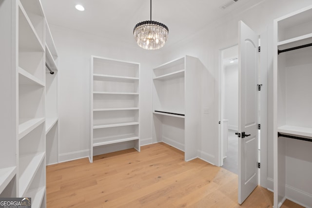 walk in closet featuring light wood-type flooring and an inviting chandelier