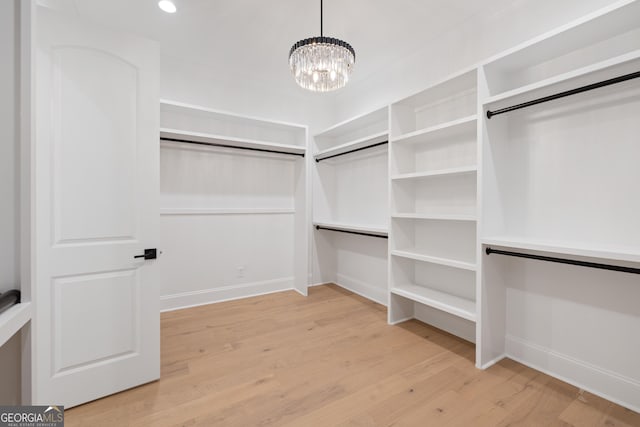 walk in closet with light wood-type flooring and a notable chandelier