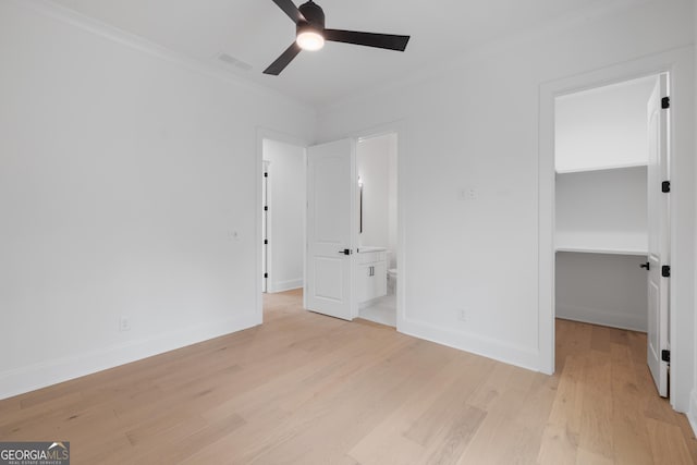 unfurnished bedroom with light wood finished floors, baseboards, a walk in closet, and crown molding