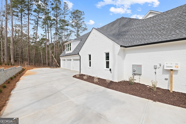 view of side of property featuring concrete driveway, brick siding, and roof with shingles