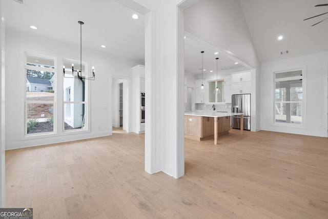 unfurnished living room with light wood-type flooring, vaulted ceiling, a notable chandelier, and recessed lighting