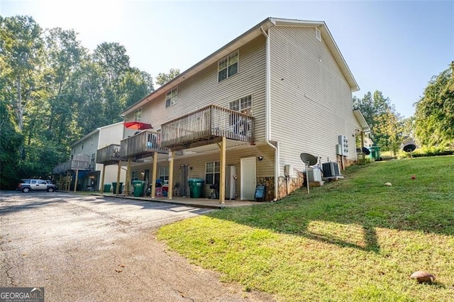 rear view of property with a lawn, central AC unit, and a deck