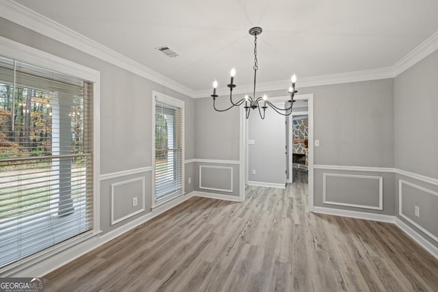 unfurnished dining area with hardwood / wood-style floors, ornamental molding, plenty of natural light, and a notable chandelier