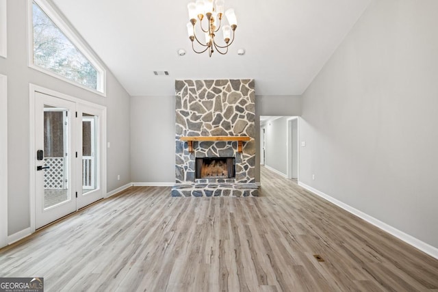 unfurnished living room with a stone fireplace, hardwood / wood-style floors, high vaulted ceiling, and an inviting chandelier