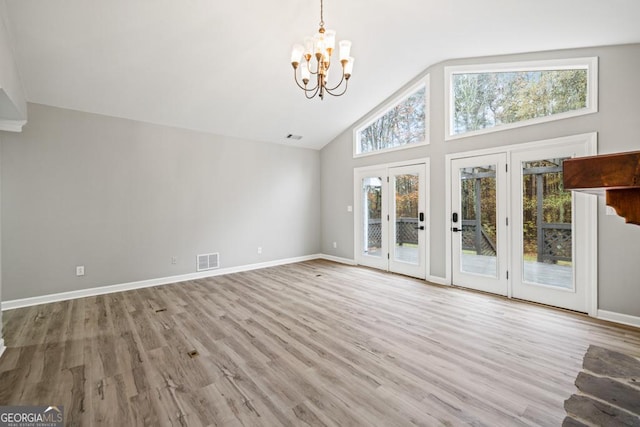 unfurnished living room with a chandelier, light wood-type flooring, high vaulted ceiling, and french doors