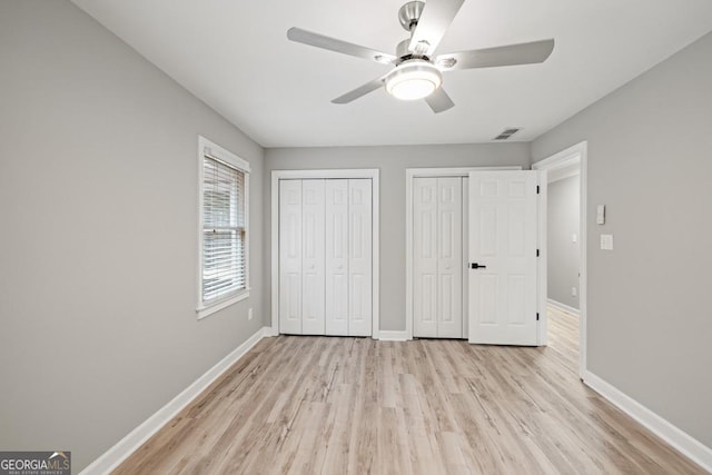 unfurnished bedroom with ceiling fan, two closets, and light wood-type flooring