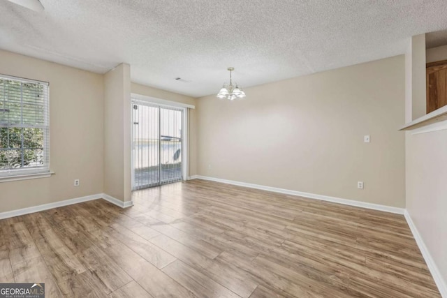 spare room with hardwood / wood-style floors, a healthy amount of sunlight, and a notable chandelier