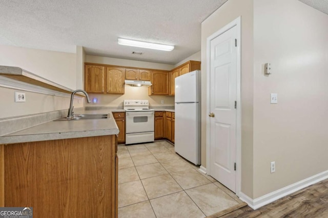 kitchen with a textured ceiling, white appliances, light tile patterned floors, and sink