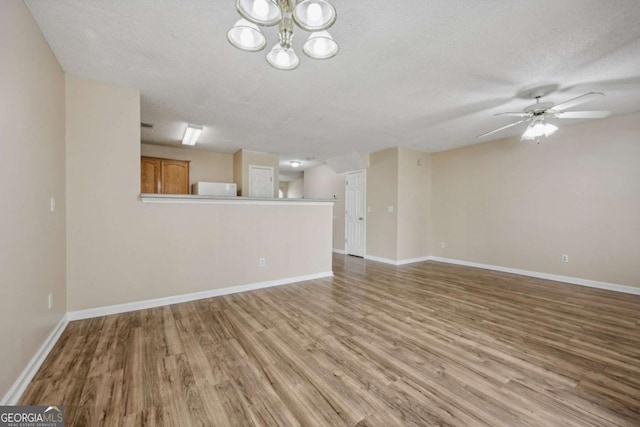 unfurnished living room featuring ceiling fan with notable chandelier, a textured ceiling, and light hardwood / wood-style flooring