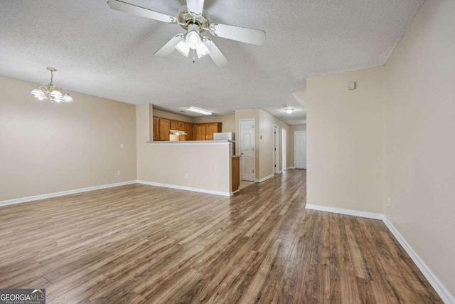 unfurnished living room with ceiling fan with notable chandelier, a textured ceiling, and light wood-type flooring