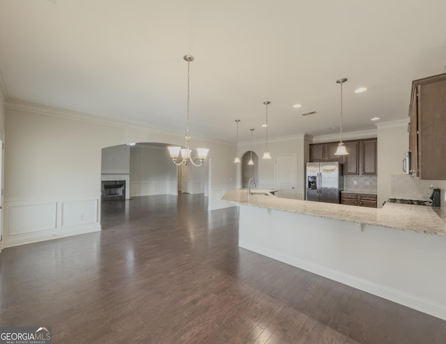 kitchen with decorative backsplash, appliances with stainless steel finishes, light stone counters, dark wood-type flooring, and pendant lighting