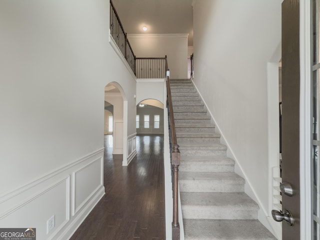 stairs with hardwood / wood-style floors, ornamental molding, and a high ceiling