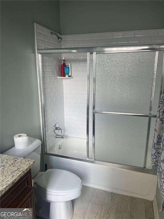 full bathroom with shower / bath combination with glass door, vanity, wood-type flooring, and toilet