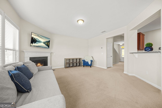 living area with light carpet, visible vents, baseboards, and a glass covered fireplace