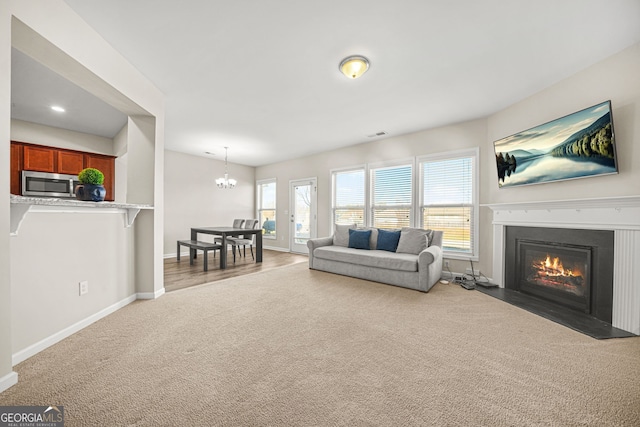 living room with visible vents, baseboards, a fireplace with flush hearth, carpet floors, and a chandelier