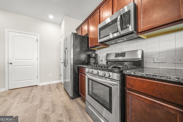 kitchen featuring stainless steel appliances, light wood-style flooring, backsplash, dark stone countertops, and baseboards