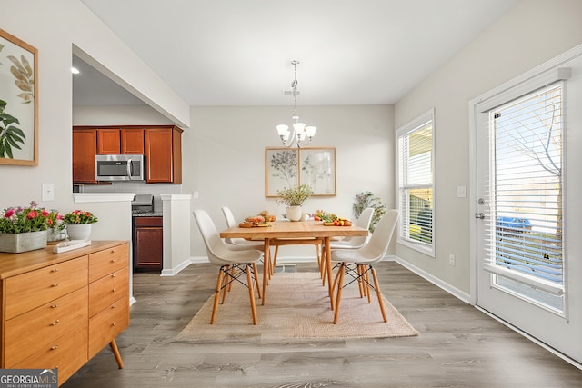 dining area with baseboards, light wood-type flooring, and an inviting chandelier