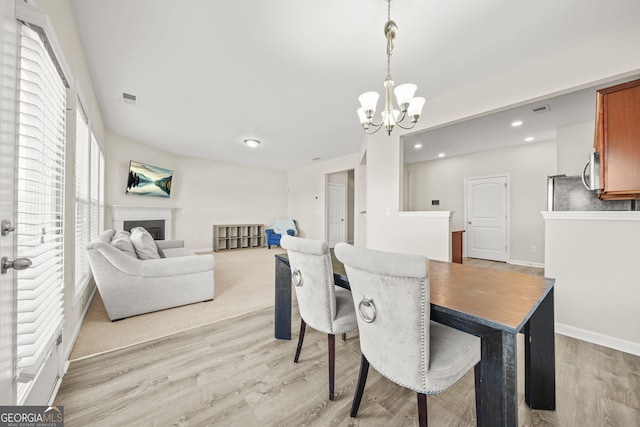 dining room with baseboards, visible vents, light wood-style floors, a fireplace, and a notable chandelier