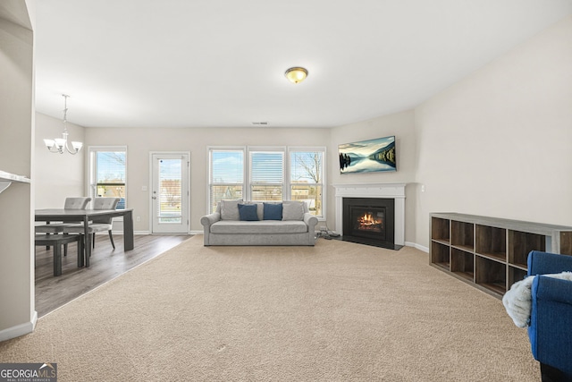 carpeted living room with a fireplace with flush hearth, a notable chandelier, and baseboards