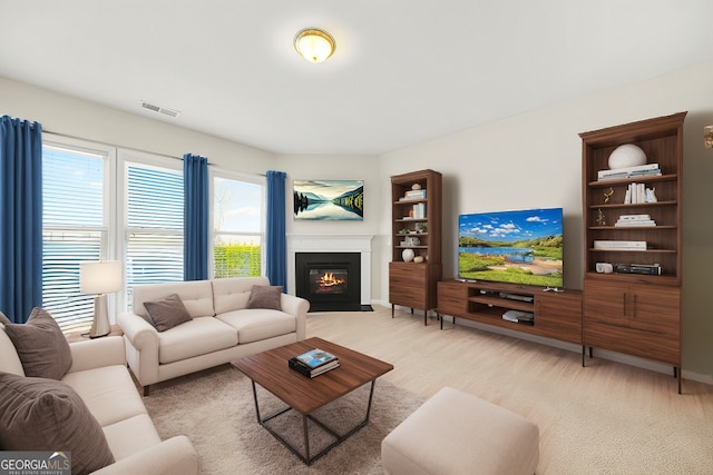 living area with light carpet, a fireplace with flush hearth, and visible vents