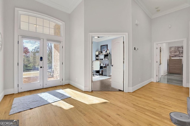 foyer entrance with wood-type flooring, crown molding, a high ceiling, and french doors