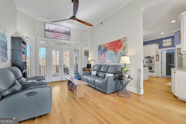 living room with french doors, light wood-type flooring, ceiling fan, crown molding, and stacked washer and dryer