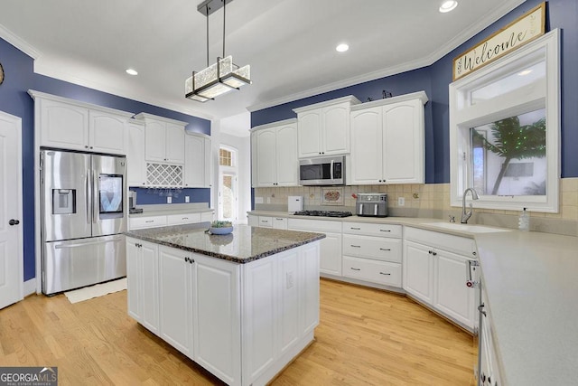 kitchen featuring appliances with stainless steel finishes, sink, decorative light fixtures, a center island, and white cabinetry