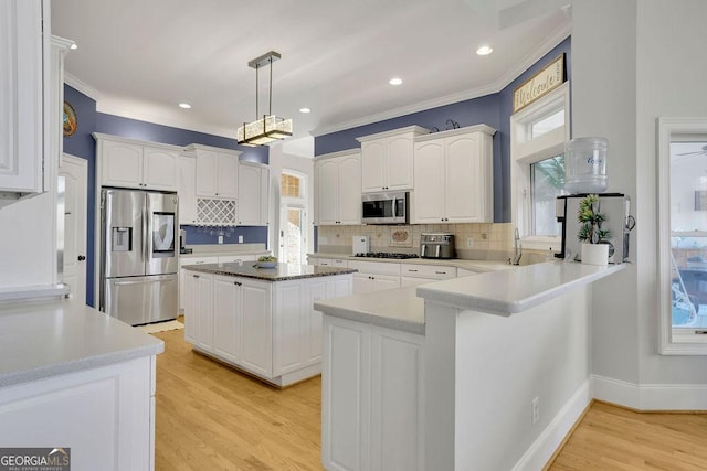 kitchen featuring kitchen peninsula, appliances with stainless steel finishes, light wood-type flooring, and decorative light fixtures