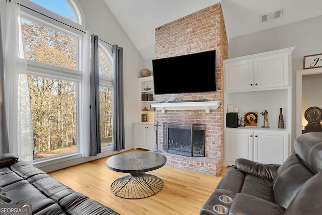 living room featuring built in features, light wood-type flooring, a brick fireplace, and lofted ceiling